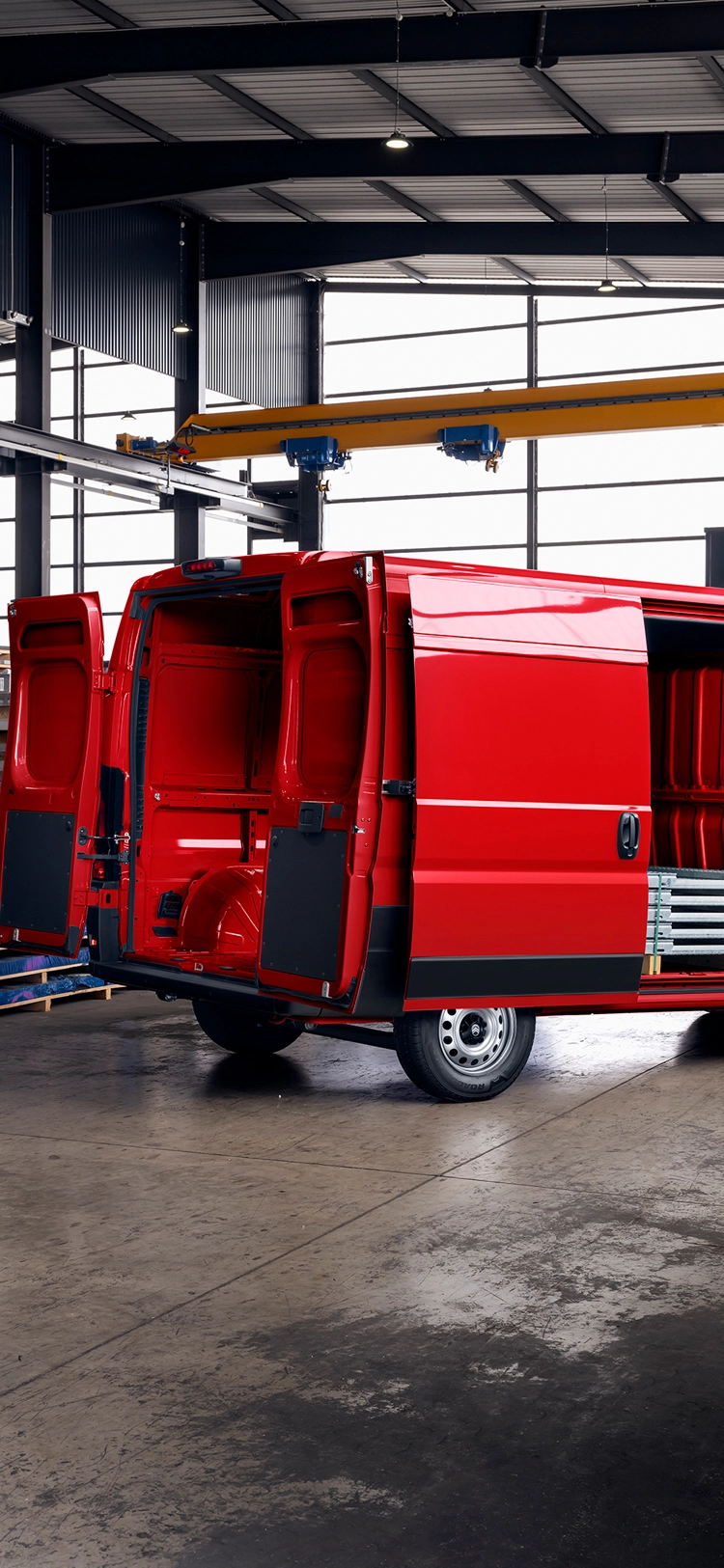 Vue arrière trois-quarts d’un Citroën Jumper rouge, portes de chargement ouvertes dans un entrepôt, mettant en avant l’espace de chargement, la durabilité et la polyvalence professionnelle.