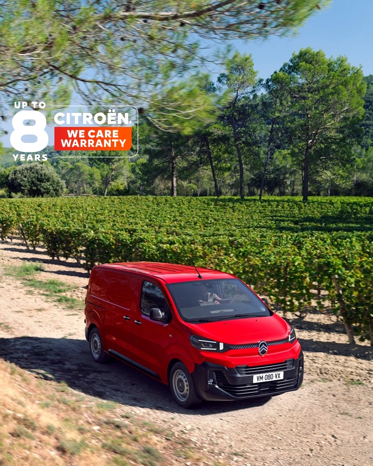 Vue extérieure en trois-quarts latérale d’un Citroën Jumpy rouge en charge devant un bâtiment, illustrant un design électrique moderne, une praticité au quotidien, la connectivité et une présence professionnelle affirmée.