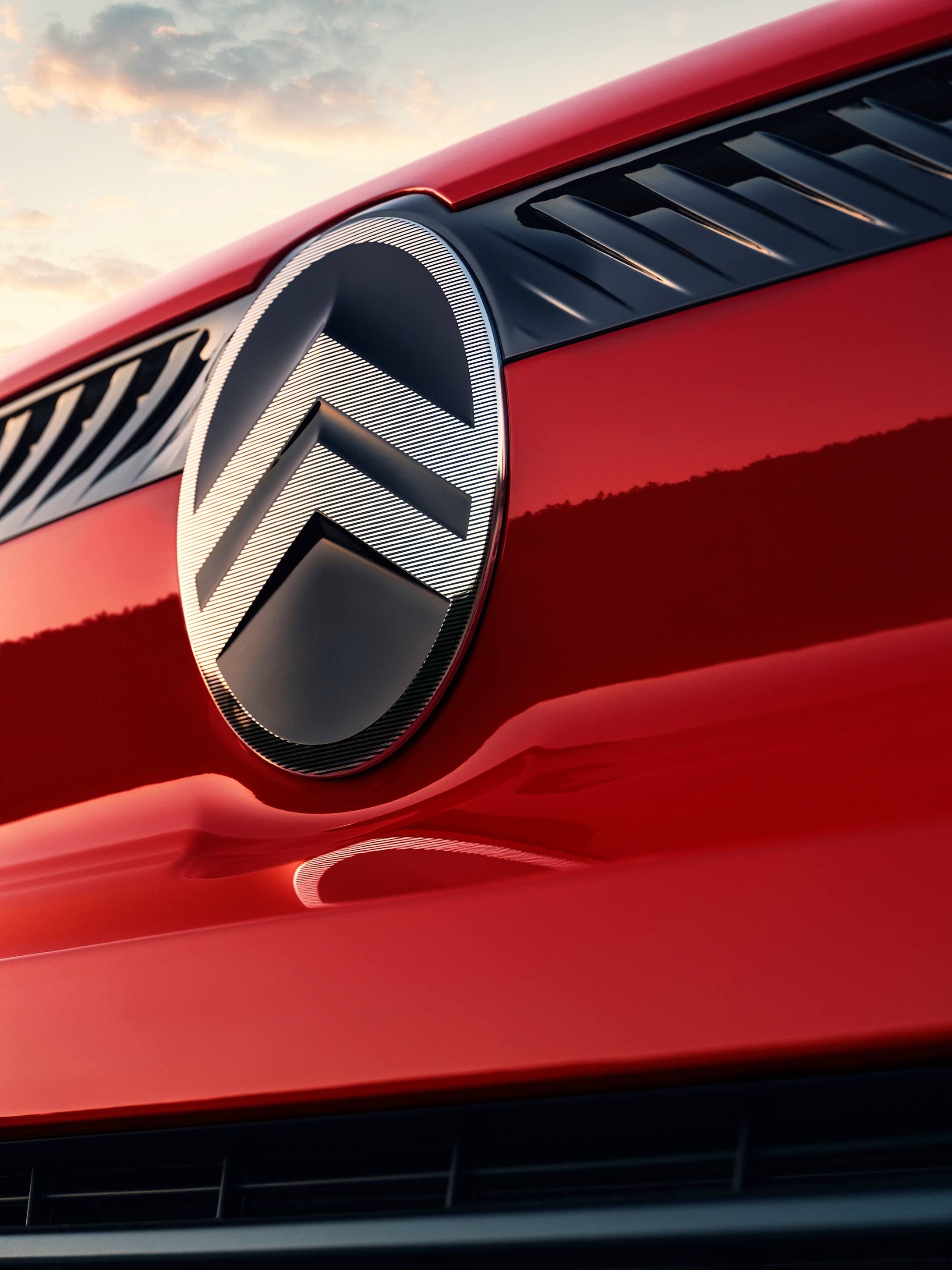 Vue extérieure en gros plan du logo Citroën sur un Citroën Jumpy rouge, mettant en avant l’identité de marque et des détails de design contemporains.
