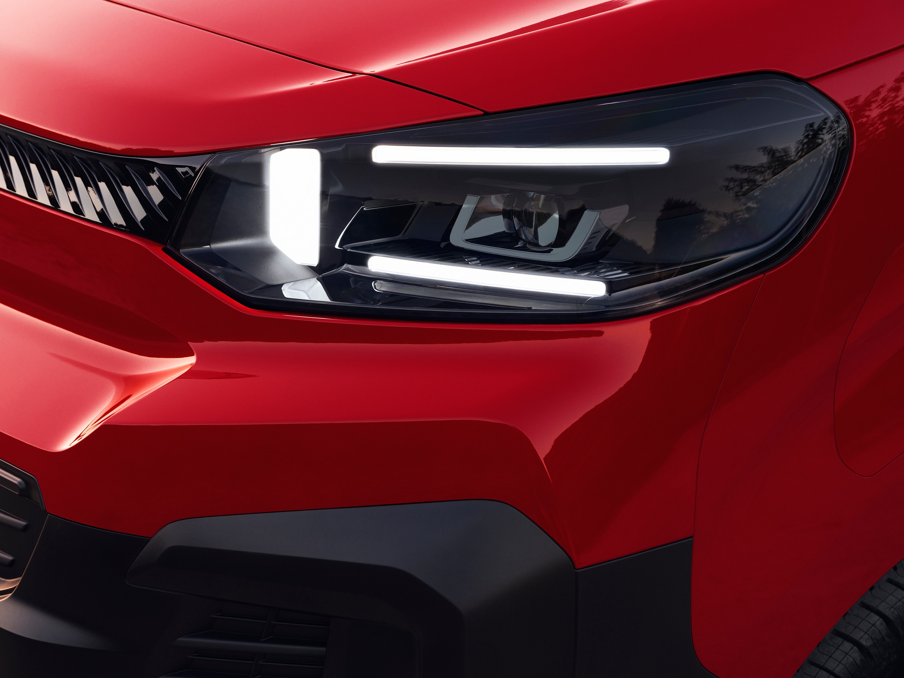 Vue extérieure en gros plan du projecteur avant d’un Citroën Jumpy rouge, illustrant un design lumineux moderne et un style robuste.