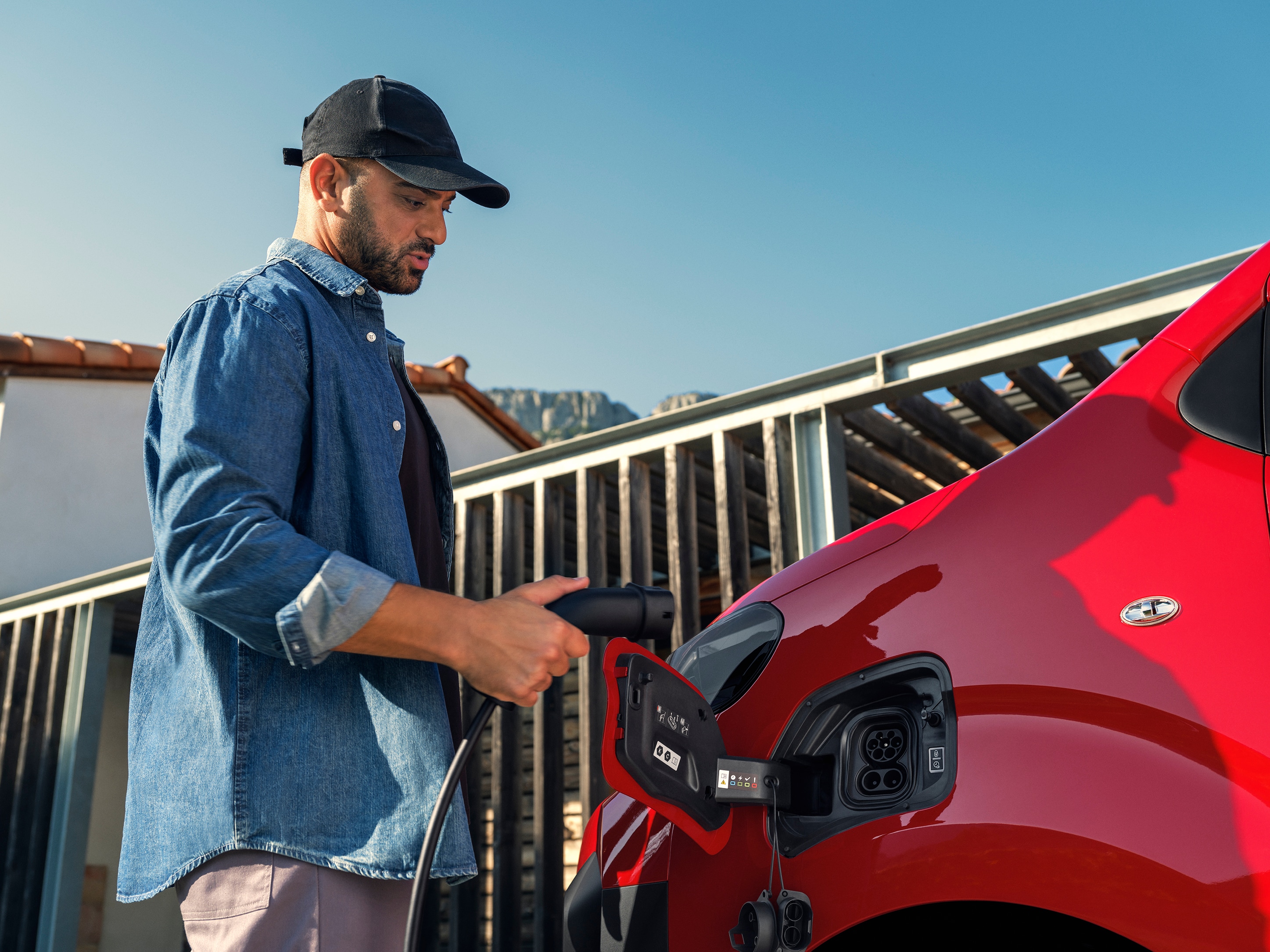 Vue extérieure latérale d’un Citroën ë-Jumpy rouge branché à une borne de recharge, illustrant une recharge simple, une utilisation connectée et une mobilité professionnelle efficace.
