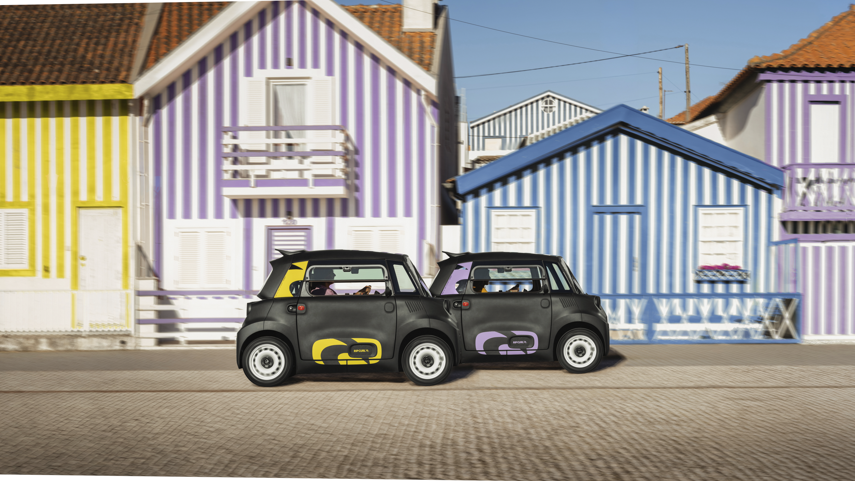 Vue de rue côte à côte de la Citroën Ami x Rip Curl électrique sans permis, style double Citroën Ami pour une voiture électrique urbaine