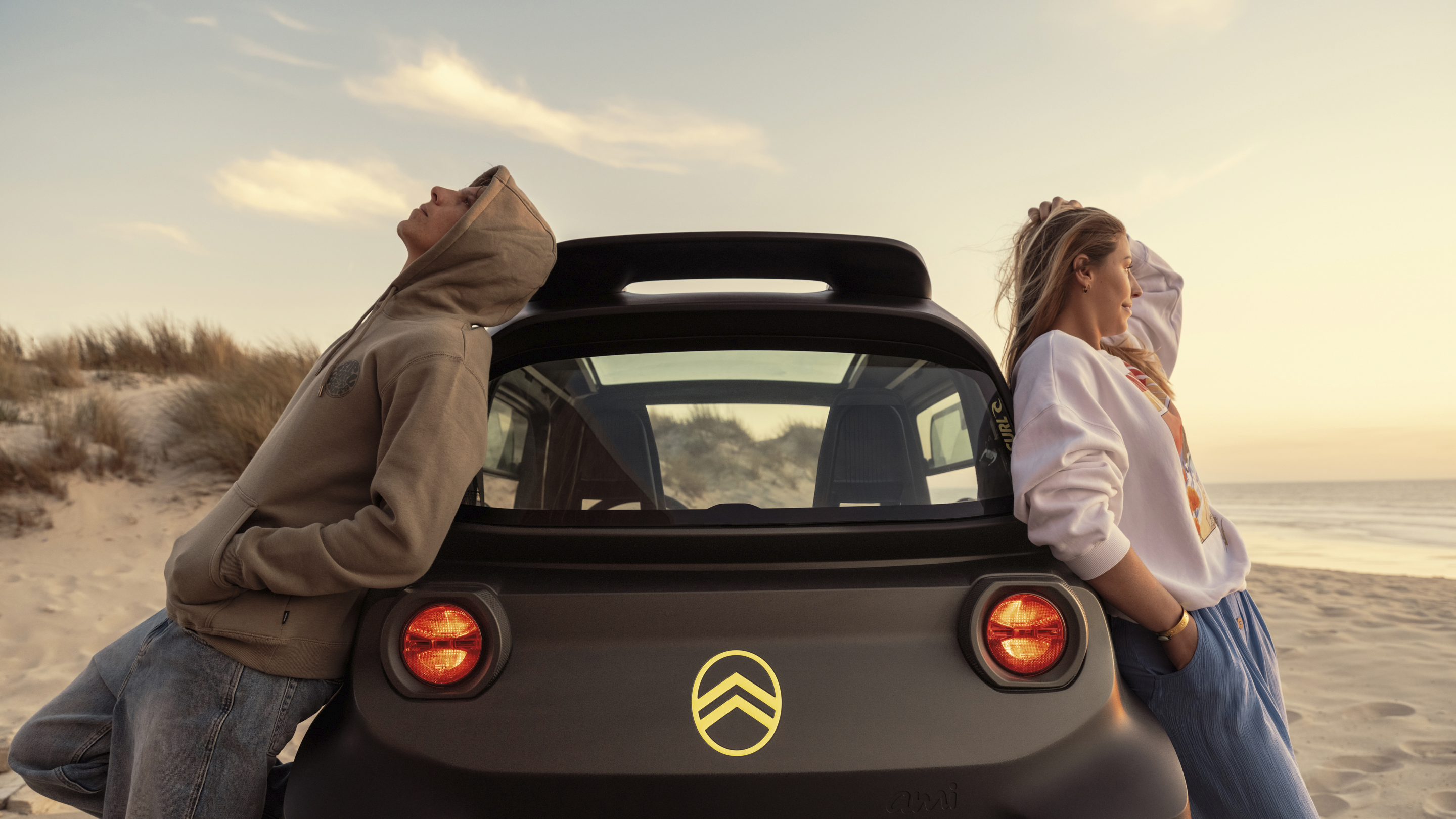 Vue arrière lifestyle au coucher du soleil de la Citroën Ami x Rip Curl électrique sans permis, Citroën Ami synonyme de liberté décontractée pour une voiture électrique urbaine