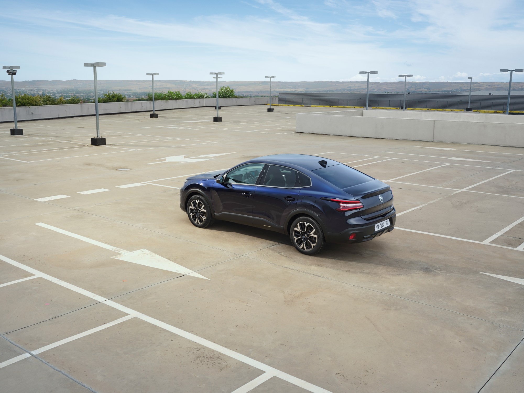 Vue arrière trois quarts de la Citroën ë-C4 X sur un parking ouvert sur le toit, mettant en valeur des lignes fastback élégantes pour une mobilité abordable